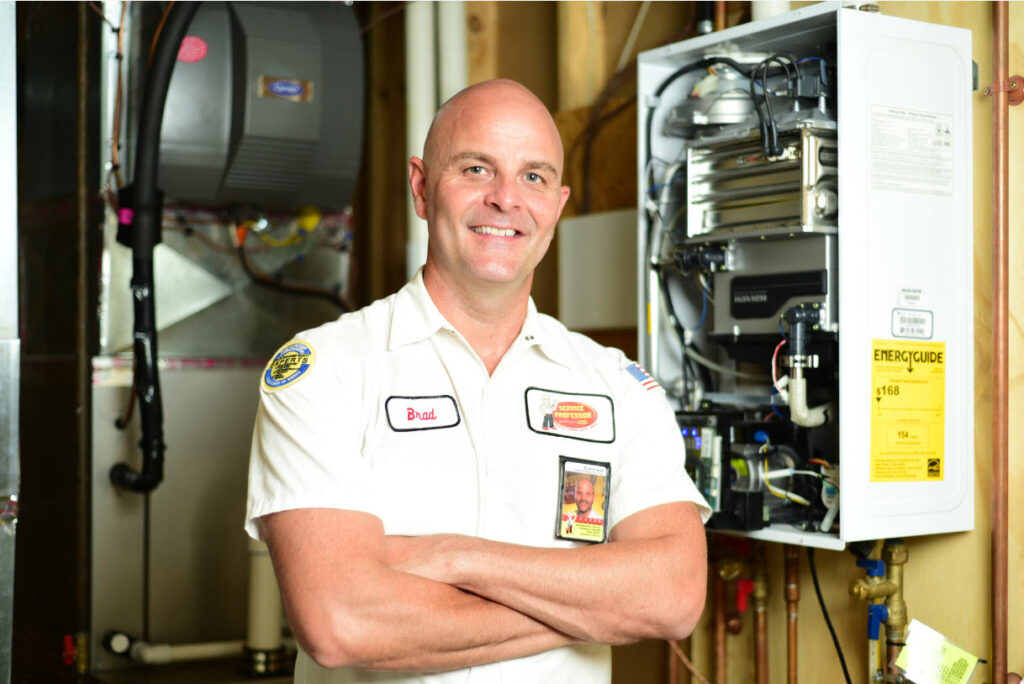 Service Professor plumber in front of a tankless water heater