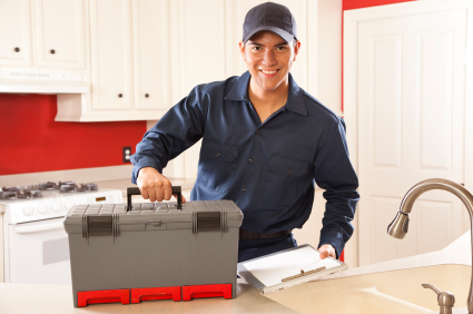 A plumber standing by a sink, smiling, with toolbox on the counter.