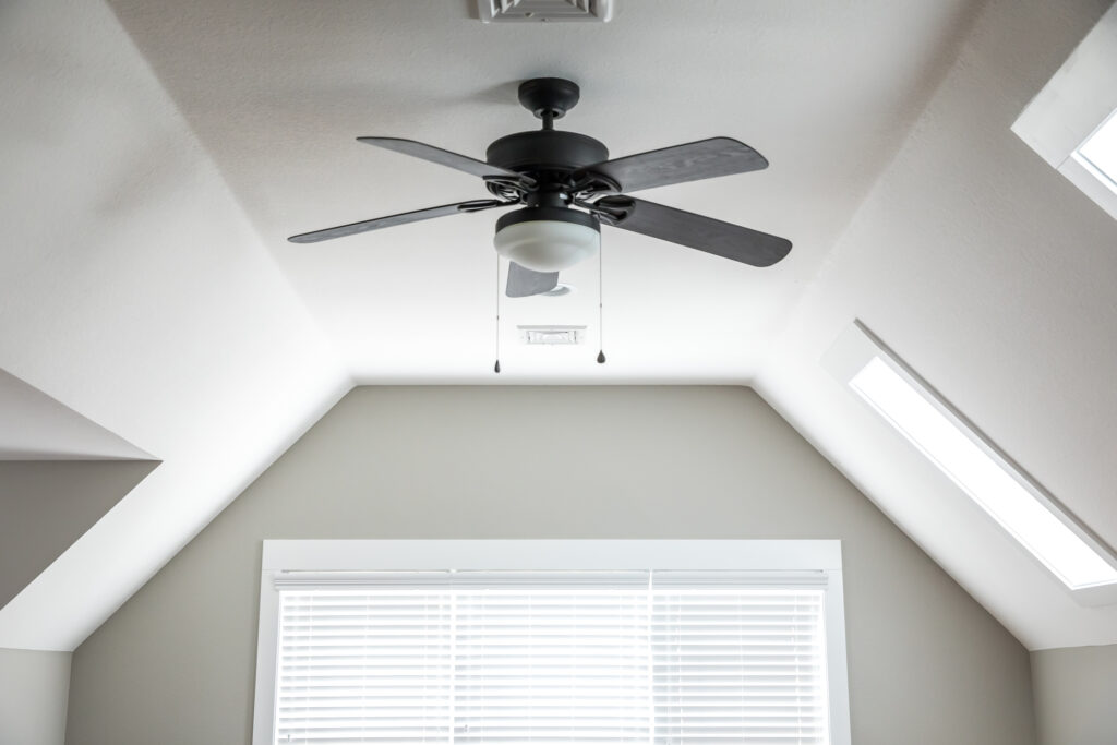 A black ceiling fan in an upstairs room with white walls.