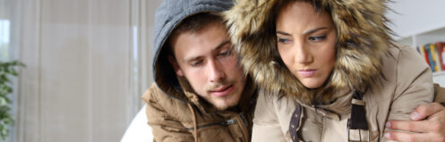 Cold home with an angry couple warmly clothed hugging sitting on a sofa in the living room